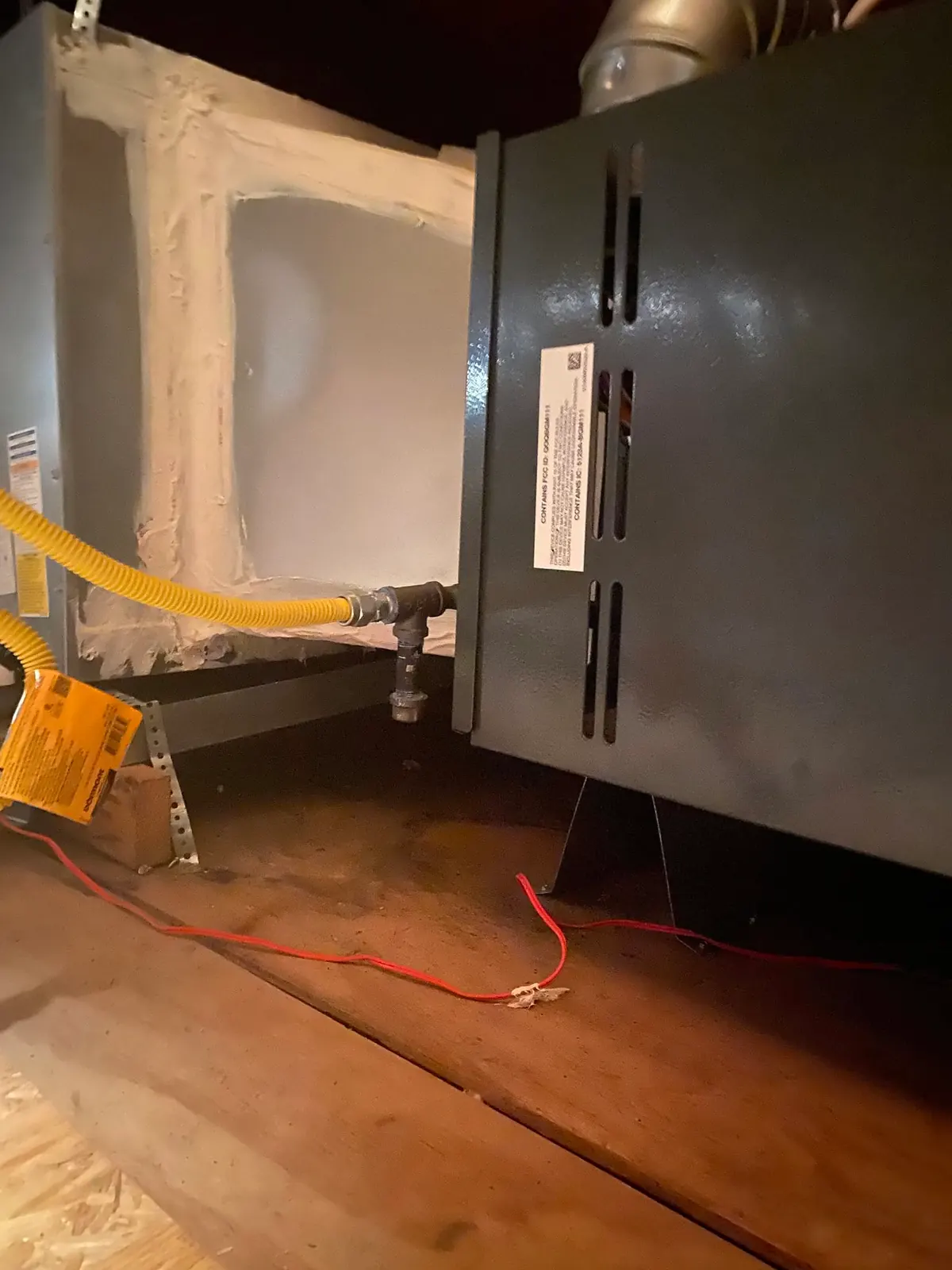 Gas furnace installed in an attic, with a yellow flex gas connector and a black-iron drip leg beside the cabinet