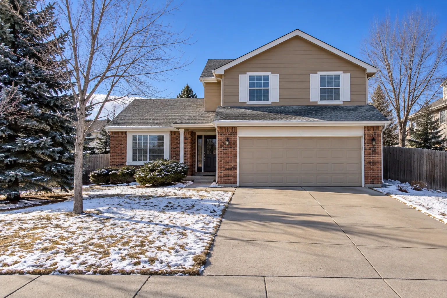 Two-story tan and brick Centennial, CO home with light snow under a blue winter sky, a home we serve for furnace repair