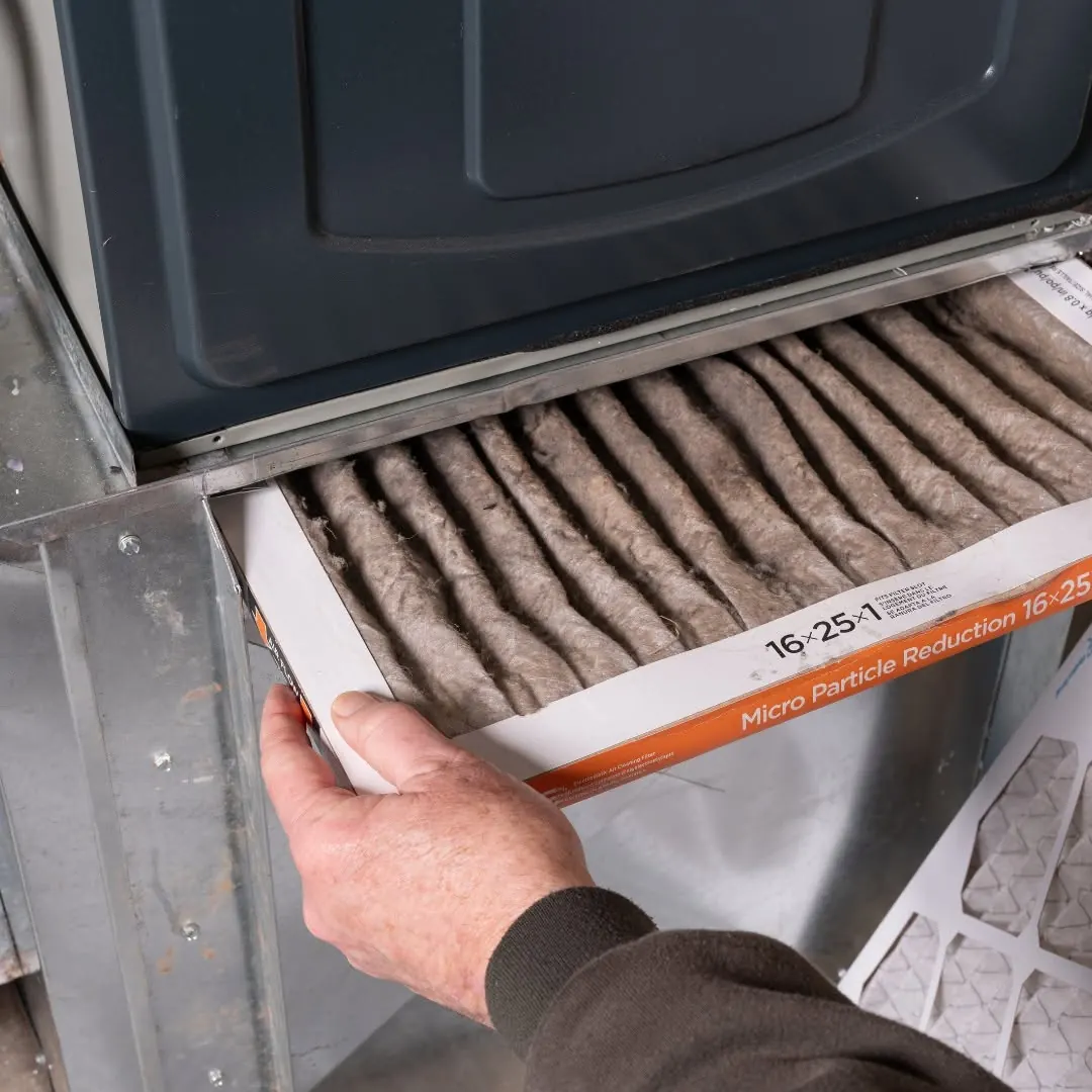 Hand pulling a dirty pleated filter from a furnace, a common cause of short cycling we check on furnace repair calls.