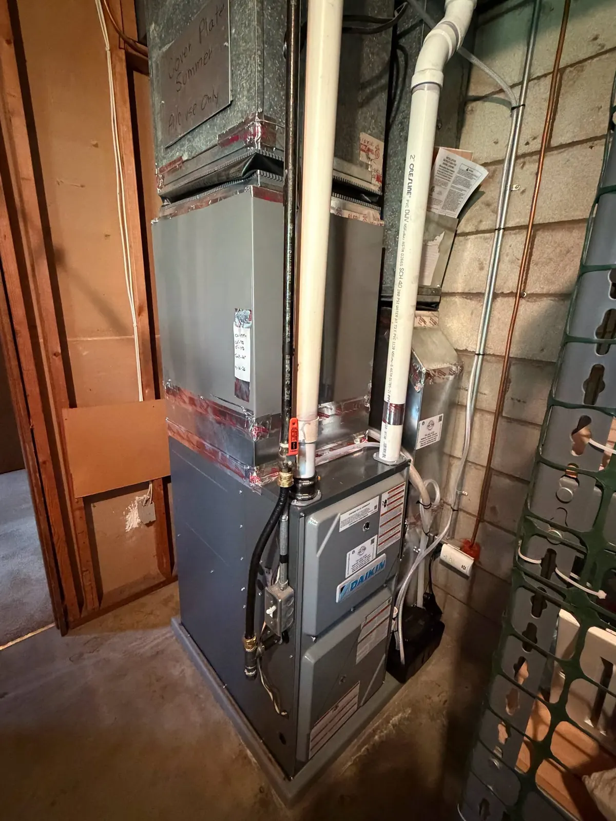 New high-efficiency gas furnace with white PVC venting and a sealed plenum in a basement after a furnace replacement.